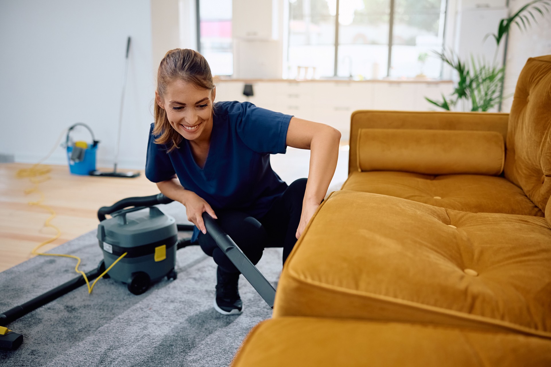 Happy housemaid using vacuum cleaner while cleaning sofa.